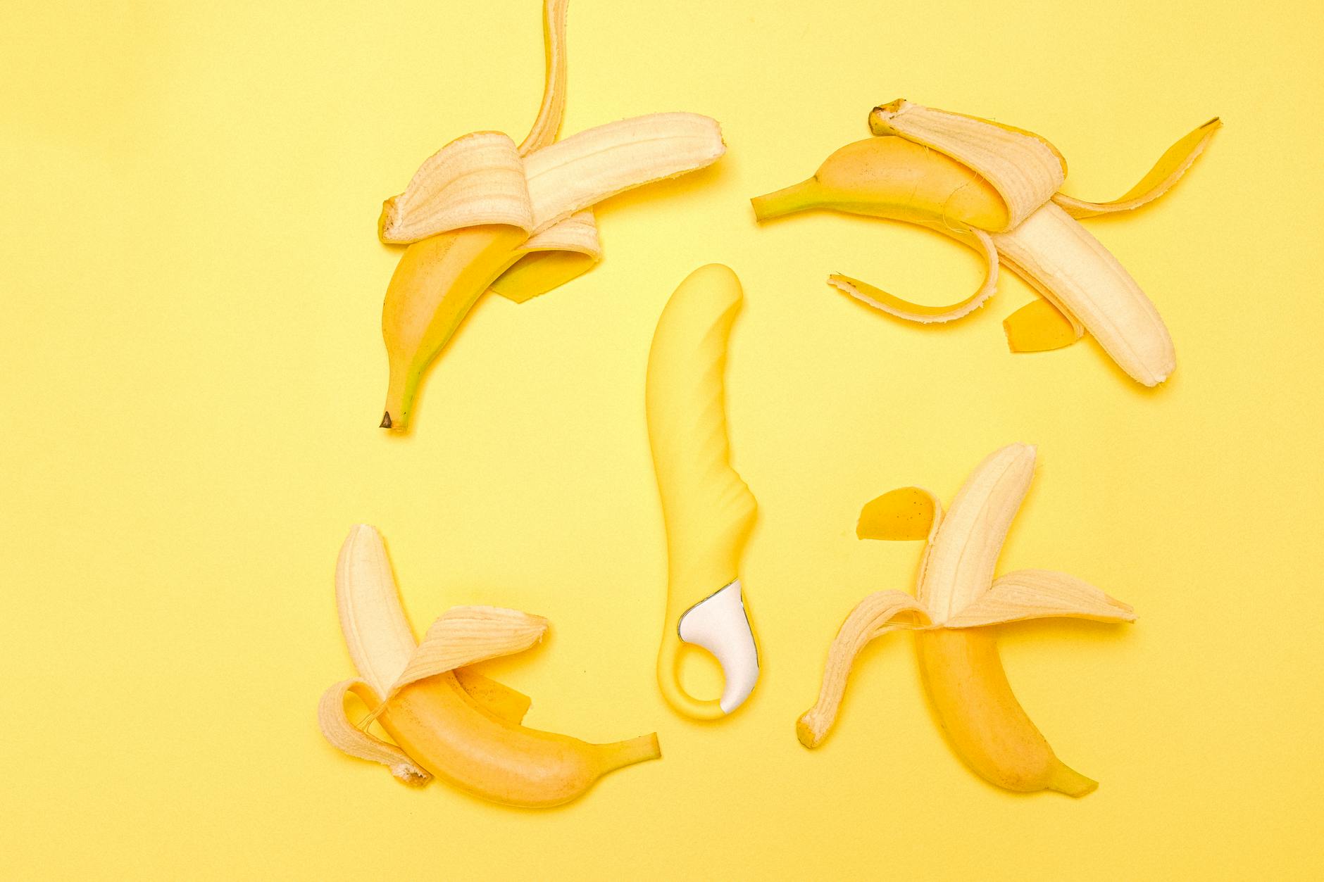 A yellow silicone lemon vibrator surrounded by peeled bananas on a yellow background, representing fresh pleasure and self-discovery.