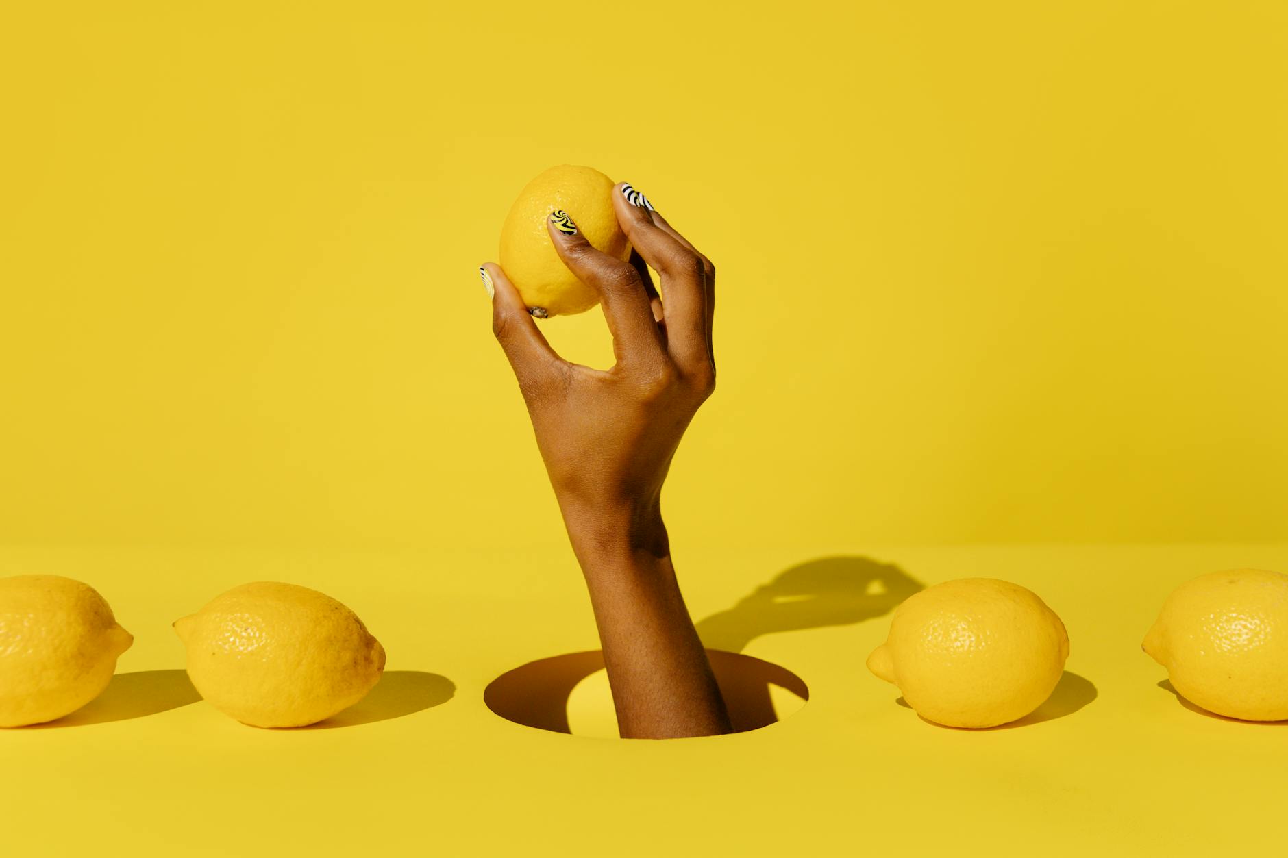 A hand holding a fresh lemon against a bright yellow background, symbolizing simplicity and natural pleasure