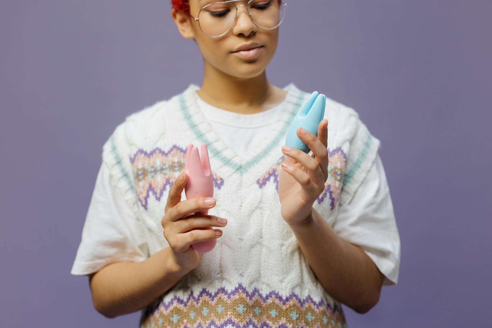 Woman with glasses thoughtfully holding a blue and pink silicone vibrator, representing the complex relationship between arousal and desire.