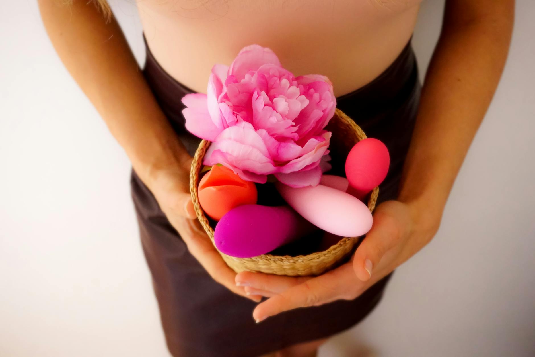 A collection of colorful vibrators in a basket with fresh flowers, representing modern sexual wellness